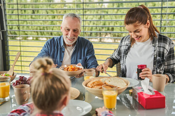 Senior man looking and little kid girl while eating tasty healthy breakfast with family