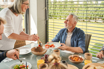 Happy senior woman having healthy lunch with her family and serving salad at dining table