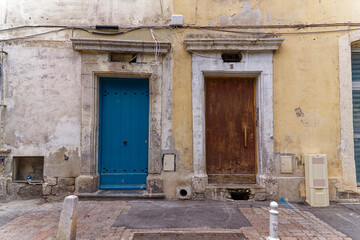 Weathered facades of houses with blue and brown wooden door with announcement to rent at French City of Toulon on a cloudy late spring day. Photo taken June 9th, 2023, Toulon, France.