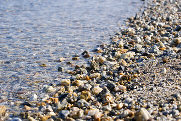 Close-up of water covered pebble beach in bright sunlight at Giens peninsula on a sunny spring day. Photo taken June 9th, 2023, Giens, Hyères, France.
