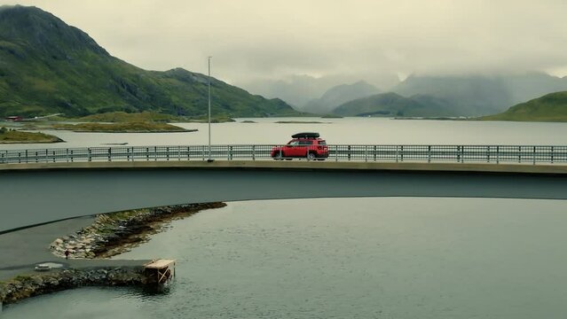 Close-up of red SUV car driving over the bridge with breathtaking fjords panorama