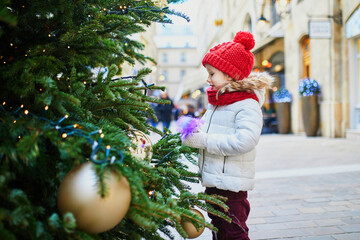 Adorable preschooler girl near Christmas trees decorated with golden baubles in Paris, France