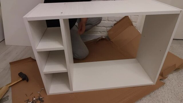 A man assembles a bookshelf on his own. Installs shelf supports..