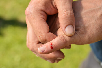 Closeup view of finger on human hand is cut hurt and bleeding with bright red blood outdoor sunny...