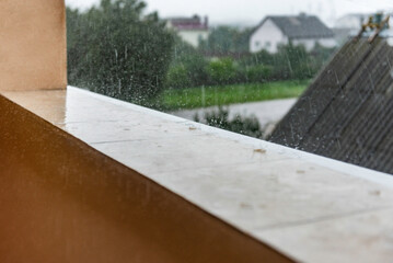 Raindrops fall on the wet tiles of an open, unglazed balcony.