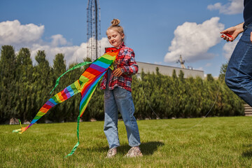 Obraz premium Little kid girl holding rainbow kite and looking on it while playing at the fresh air