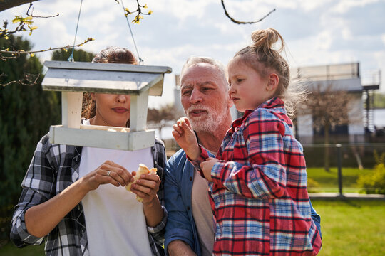 Handsome mature man holding adorable little girl in his arms while kid looking at wooden birdhouse