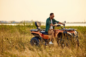 An excited man driving a rented quad bike and looking around the nature.