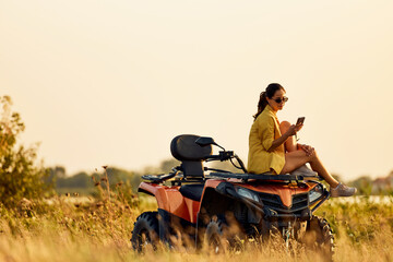 A pretty woman sitting on a quad bike during drive break, using a phone. © bnenin