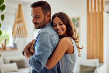 A smiling woman in love giving her boyfriend a hug from the back at home.