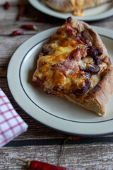Slice of pizza with kidney beans, bacon, cheese, tomatoes and onions on a plate. Tex mex food