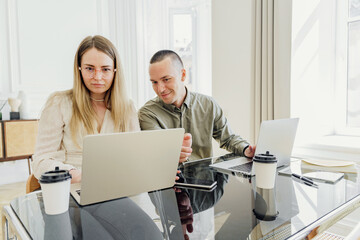A woman and a man use a laptop, an online project. Colleagues in the coworking space team are freelancers. Young startup people work in the office.