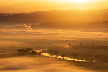 Aerial view of the sunrise over the valley in beautiful early morning mist in the highlands. Low clouds and fog cover the sleeping meadow. Hills valley mists landscape. Serene moment in rural area