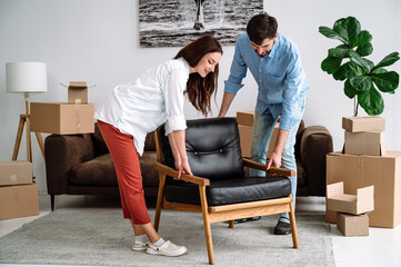 Smiling couple carrying modern chair together, arranging furniture