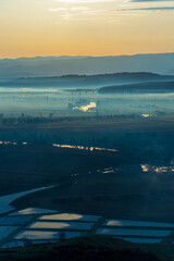 Aerial view of the valley in early morning mist, beautiful in the highlands. Low clouds and fog cover the sleeping meadow. Alpine mountain valley mists landscape at dawn. Serene moment in rural area