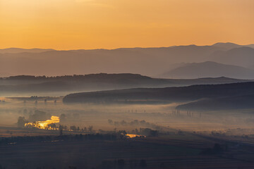 Aerial view of the valley in early morning mist, beautiful in the highlands. Low clouds and fog cover the sleeping meadow. Alpine mountain valley mists landscape at dawn. Serene moment in rural area