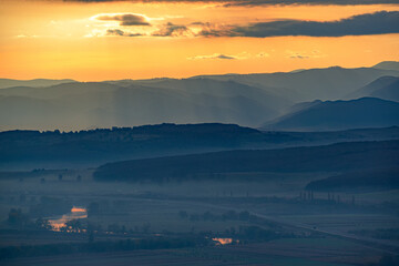 Aerial view of the valley in early morning mist, beautiful in the highlands. Low clouds and fog cover the sleeping meadow. Alpine mountain valley mists landscape at dawn. Serene moment in rural area