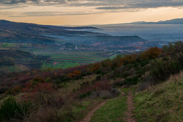 Serene moment in rural area in beautiful autumn early morning mist. Panoramic view of a sleeping meadow valley covered with low clouds and fog, village hiding between rolling hills covered with trees