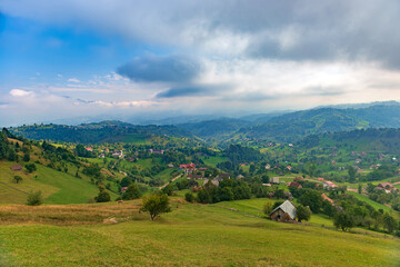 Fototapeta na wymiar Rural idyllic landscape of the small villages in the Rucar-Bran mountain area, Brasov, Romania, scattered on the wooded hills, with the Bucegi mountains in the background, in wonderful springtime day