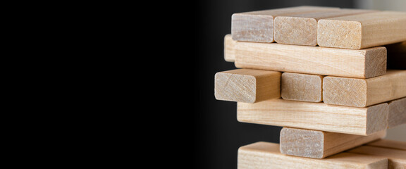 Wood block unstable staking. Wooden blocks tower with copy space on black background.