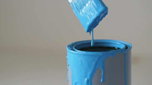 Close-up view on brush with blue paint. Large drops drain into a can of paint. Studio shooting with hand-held camera.
