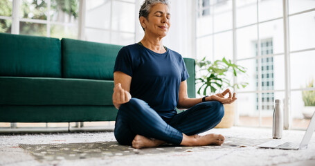 Practicing yoga in retirement: Healthy senior woman meditating in lotus position at home
