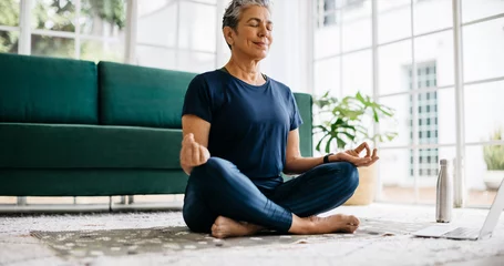 Fototapeten Practicing yoga in retirement: Healthy senior woman meditating in lotus position at home © (JLco) Julia Amaral