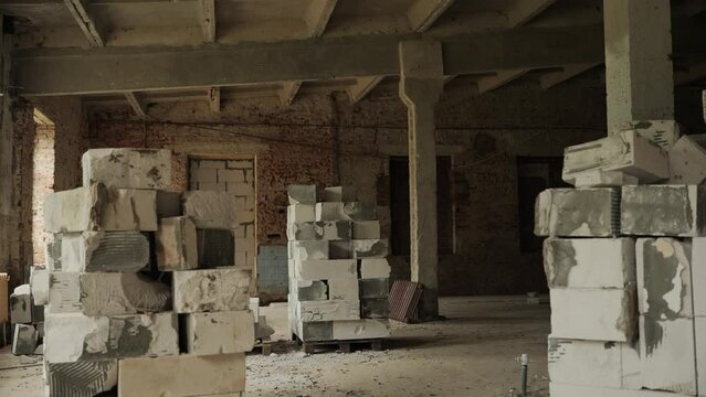 The camera moves from left to right in a destroyed spacious industrial building, which is being renovated. Several pallets with destroyed building blocks on the construction site. High quality 4k