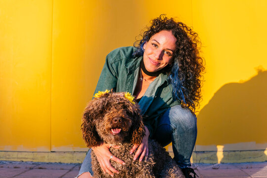 Smiling young woman crouching with water dog in front of yellow wall