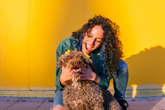 Happy woman playing with water dog in front of yellow wall