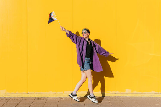 Carefree lesbian woman jumping with rainbow flag in front of yellow wall