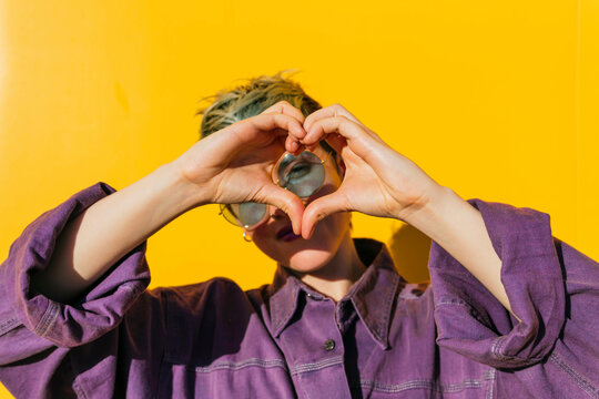 Woman making heart gesture in front of yellow wall