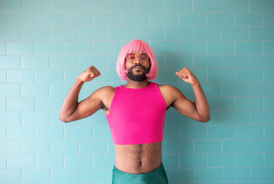 Young queer man flexing muscles standing in front of wall