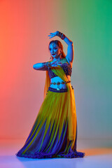 Odissi dance. Beautiful young woman in traditional dress dancing against gradient studio background in neon light. Concept of beauty, fashion, India, traditions, lifestyle, choreography, art. Ad