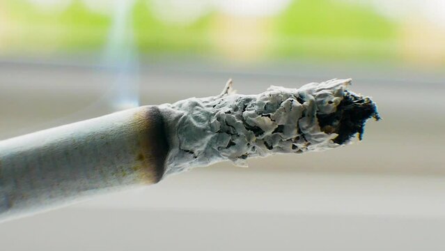 A cigarette smokes near the window, smoking a cigarette macro shot, on a gray bokeh background, a smoking cigar close-up.