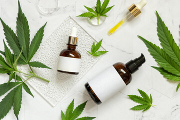 Cosmetic bottles with blank label near green cannabis leaves on marble table top view. Mockup