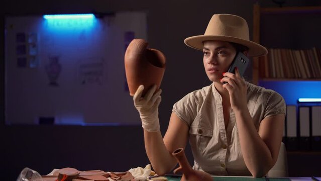 Female archaeologist discussing antique vessel with colleague works at night in office