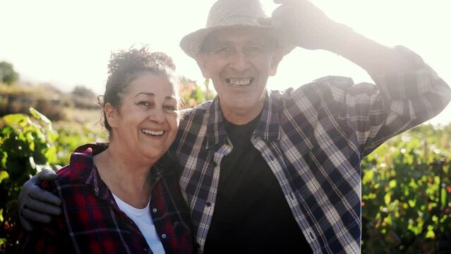 Happy senior farmer couple looking at camera with rural field farm in background - Small business agriculture and harvest concept