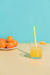 A glass of tangerine juice with a slice. Tangerines on a plate. Beige and turquoise background. copy space.