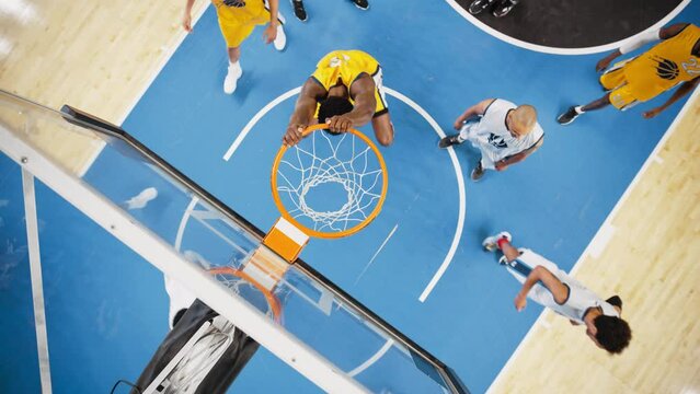 Slow Motion Cinematic Replay of Basketball Action for Live TV Channel Playback: Top Down Zoom Out Footage of an African Yellow Team Player Scores a Powerful Slam Dunk Goal and Hangs on the Hoop