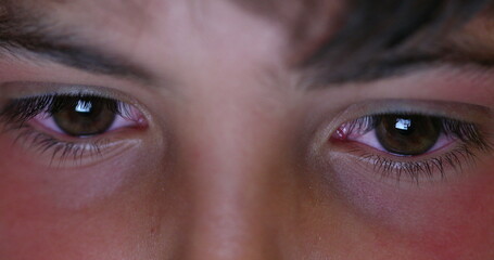 Boy macro eyes staring at screen device at night. Child browsing internet eye close-up