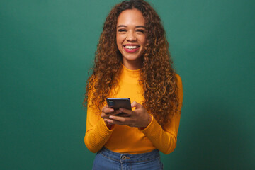 Beautiful young woman texting on cellphone, smiling, green studio background