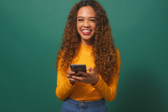Beautiful young woman texting on cellphone, smiling, green studio background - Powered by Adobe