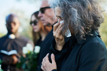 Senior woman with grey hair wiping tears with handkerchief at funeral of her relative or family...