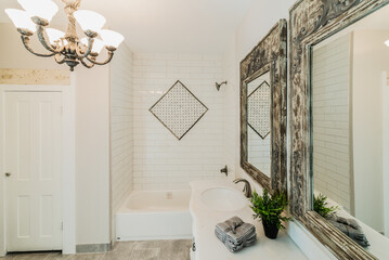 White vanity with two mirrors, two sinks, and a tub with a tile inlay