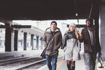 Three young multiethnic friends having fun strolling railway station