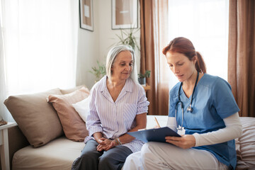 Female caregiver doing regular check-up of senior woman in her home.