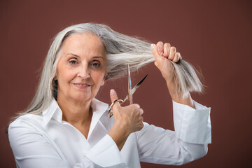 Portrait of senior woman cutting own gray hair.