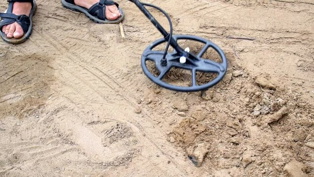 Person using electronic metal detector and scoop to find treasures in the sand. Man with equipment looking for precious objects on the beach of river or lake.