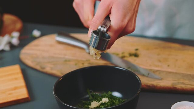 A woman squeezes garlic with a garlic press and removes the excess with a knife. Close-up of a table. Cooking in the kitchen.